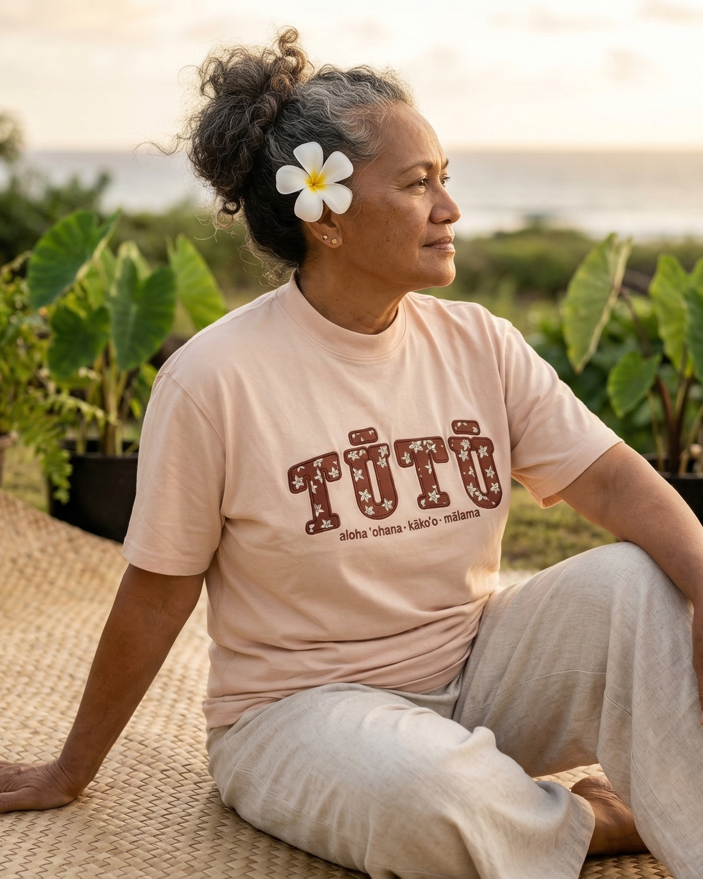 Hawaiian woman grandma sitting wearing a light pink tutu shirt. Hawaiian affirmation apparel.