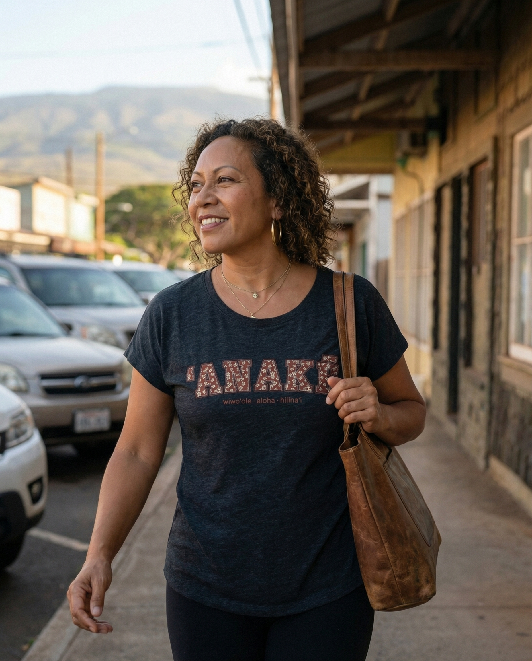 Pua Kukui ʻAnakē scoop neck tee in Vintage black, worn by woman walking through a Hawaiʻi town at golden hour.